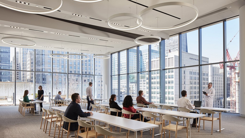 A group of people sitting at tables in a room with large windows.